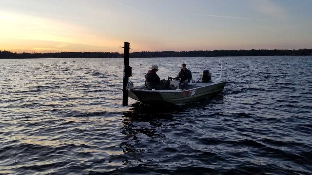 Field scientists aboard a survey boat collect environmental data on a lake during sunset.